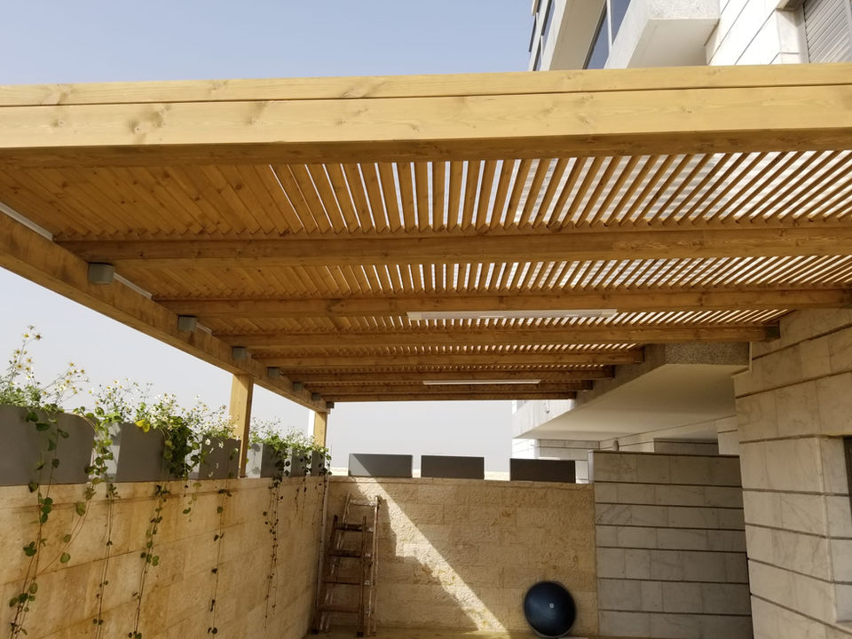  פרגולה מעץ במרפסת בצבע חום זהב או חום דבש מעל קיר מאבן וגדר עץ
