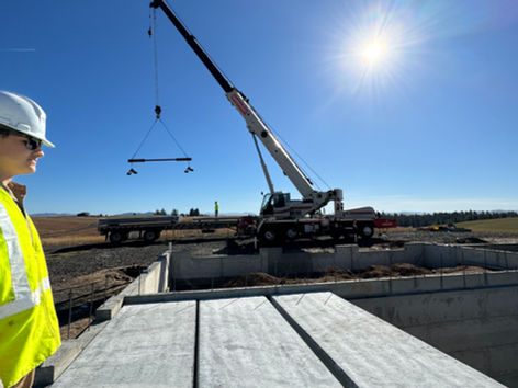 Construction worker observes a crane lifting concrete beam on a sunny day