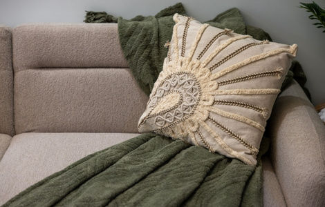 Beige sofa with a green throw blanket and a cream embroidered decorative pillow, creating a cozy, calm living room feel.