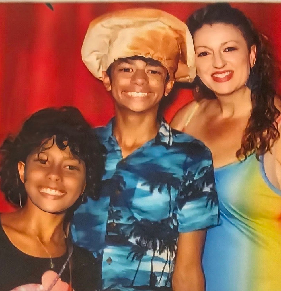 A woman and two smiling children posing in front of a red curtain