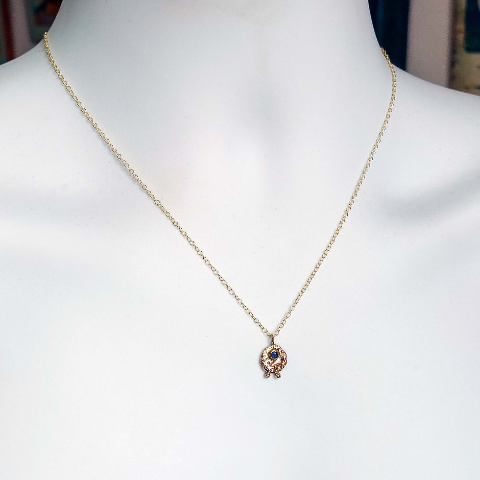 organic textured round gold pendant with two gold balls at bottom, top set with a bule sapphire