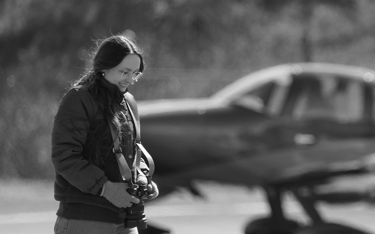 Portrait of Autumn Baugh (A. Baugh) photographing an airplane in her profession