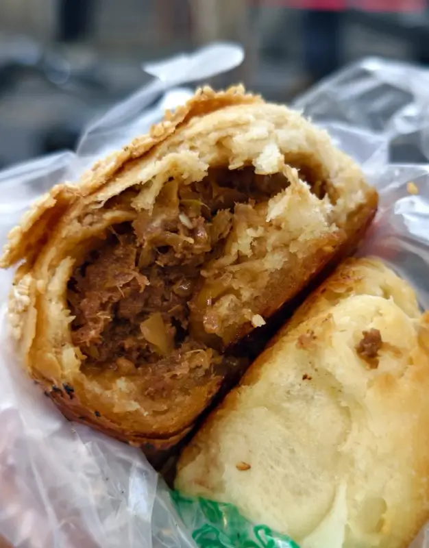 Close-up of a beef-filled shaobing from Manji on Niujie, showing its flaky crust and savory filling