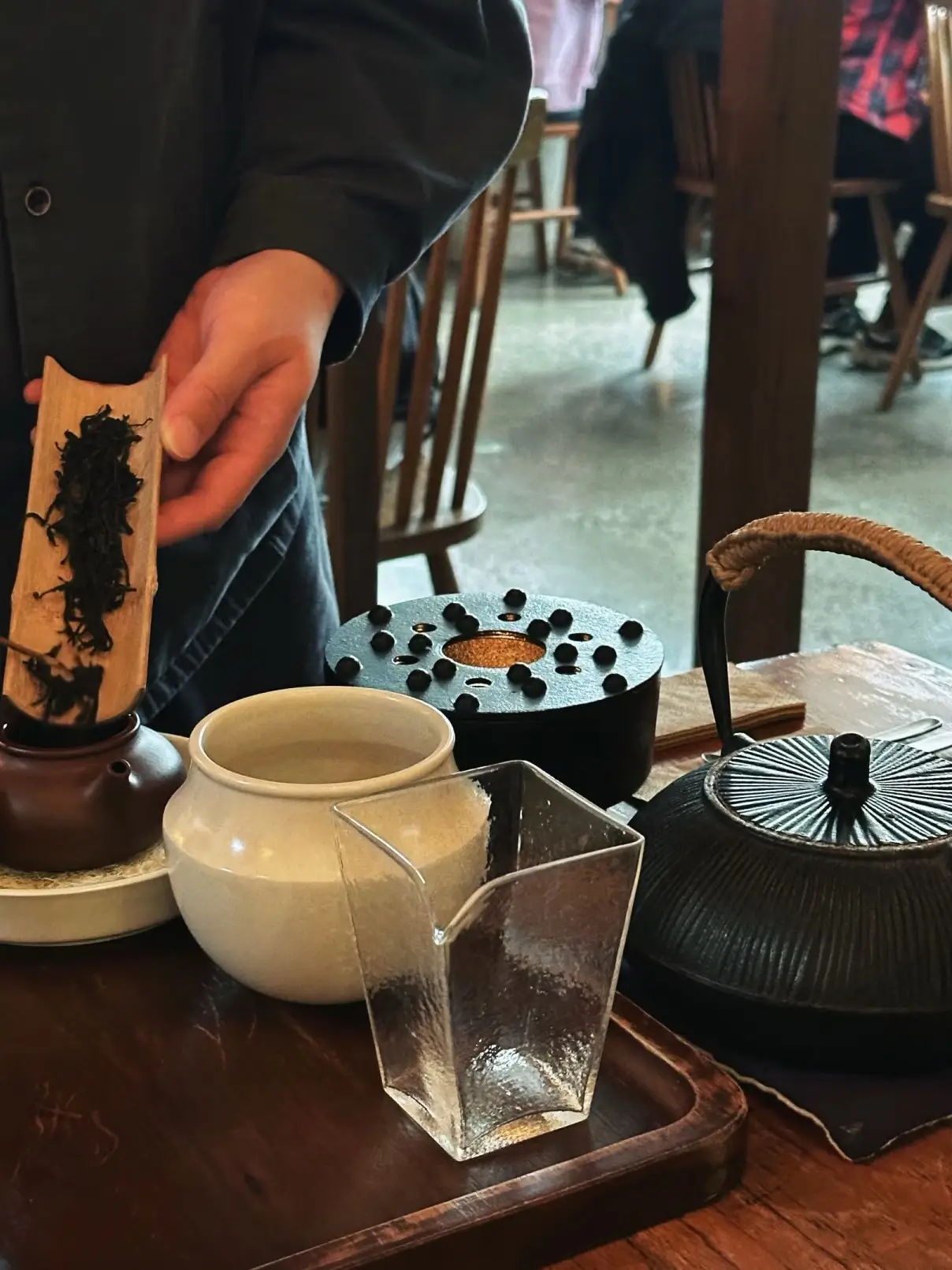 Hand holding loose tea leaves over a teapot during a Chinese tea ceremony with teaware arranged on a