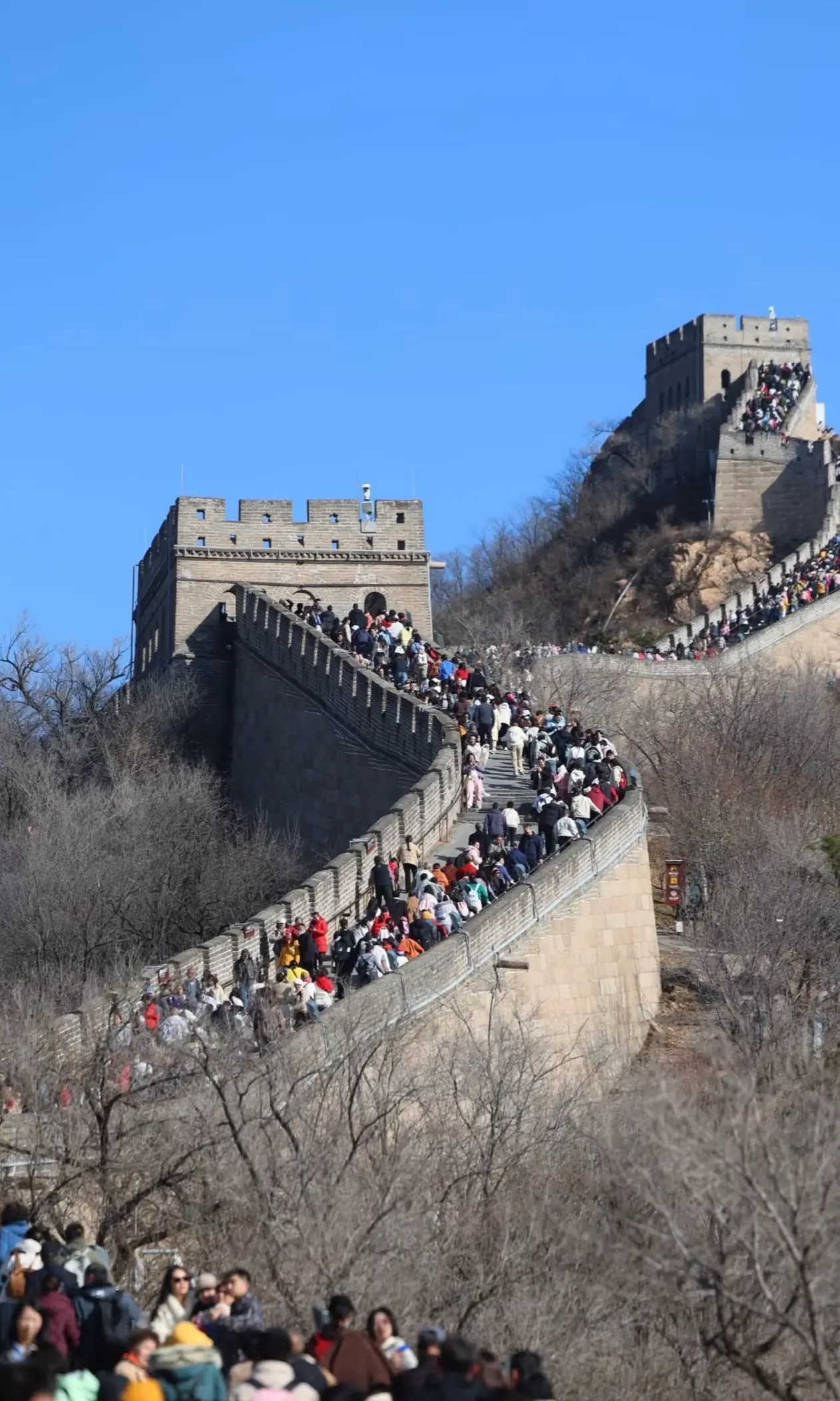 Heavy crowds of visitors climbing a steep section of the Great Wall of China on a clear day.