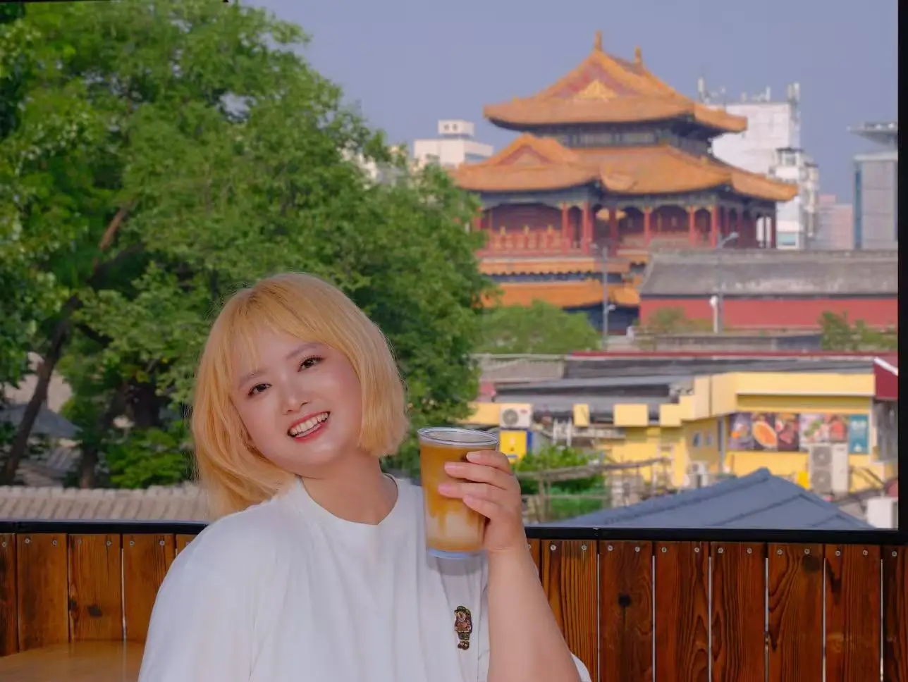 A traveler enjoying a drink on a rooftop café near Lama Temple, with traditional Beijing temple rooftops in the background.