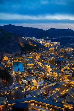 Panoramic dusk view of Gubei Water Town, with traditional Chinese architecture, lit-up canal, and surrounding mountains, showcasing the charming ancient water town for private bite escape tours.