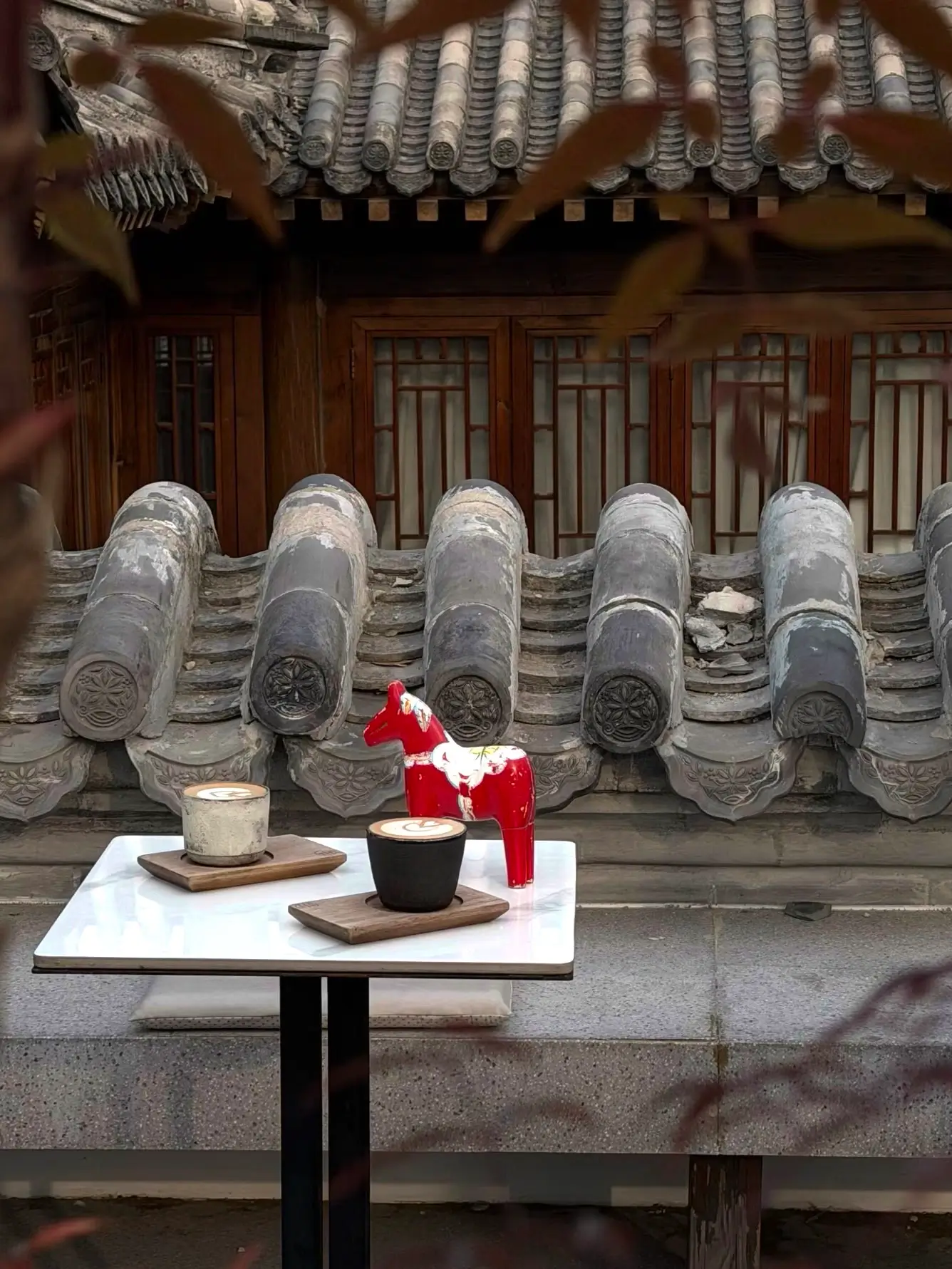 Coffee and ceramic cups placed on a small table beside traditional grey-tiled rooftops in a Beijing siheyuan courtyard.