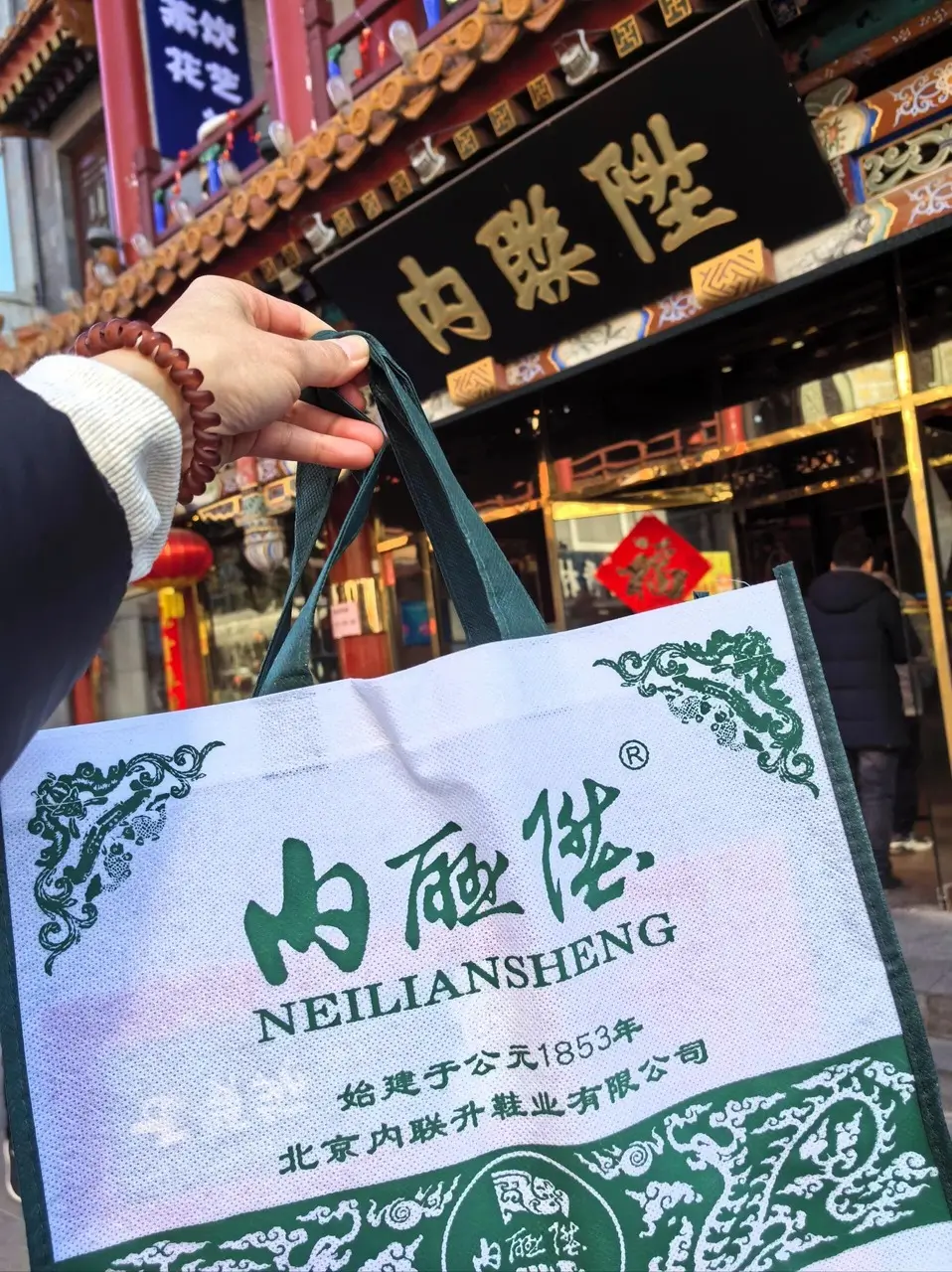 Neiliansheng shopping bag in front of a traditional Beijing storefront, highlighting the iconic time-honored cloth shoe brand.