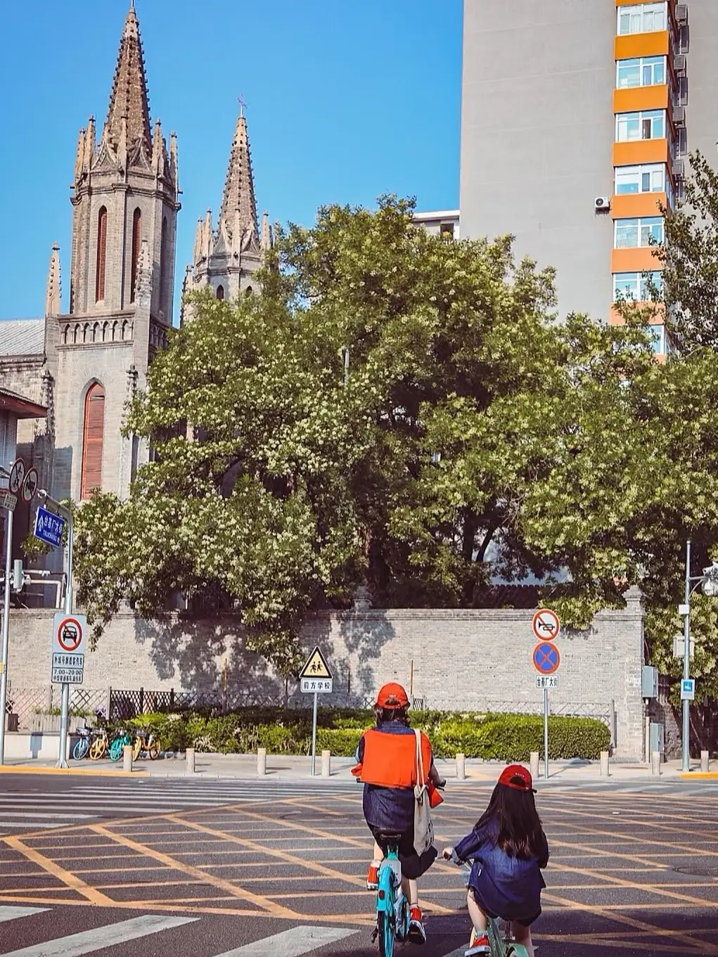St. Michael’s Church in Dongjiaominxiang, Beijing, with Gothic-style towers rising behind trees as pedestrians and cyclists move through the historic street.