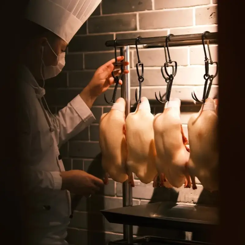 Chef roasting Peking duck in a traditional hanging oven at Quanjude