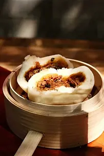 Steamed Chinese bao bun filled with savory meat, served in a bamboo basket during a Bite Escape Beijing food tour.