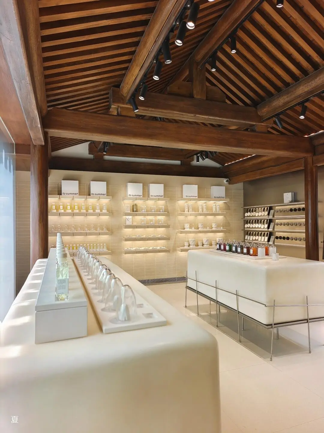 Interior of To Summer fragrance store in Beijing, featuring warm wooden beams, minimalist display tables, and shelves of Oriental botanical scent products.