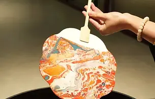 Marbled lacquer fan lifted from colored water during a BiteEscape cultural experience, showcasing unique flowing patterns created by hand.