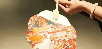 Marbled lacquer fan lifted from colored water during a BiteEscape cultural experience, showcasing unique flowing patterns created by hand.