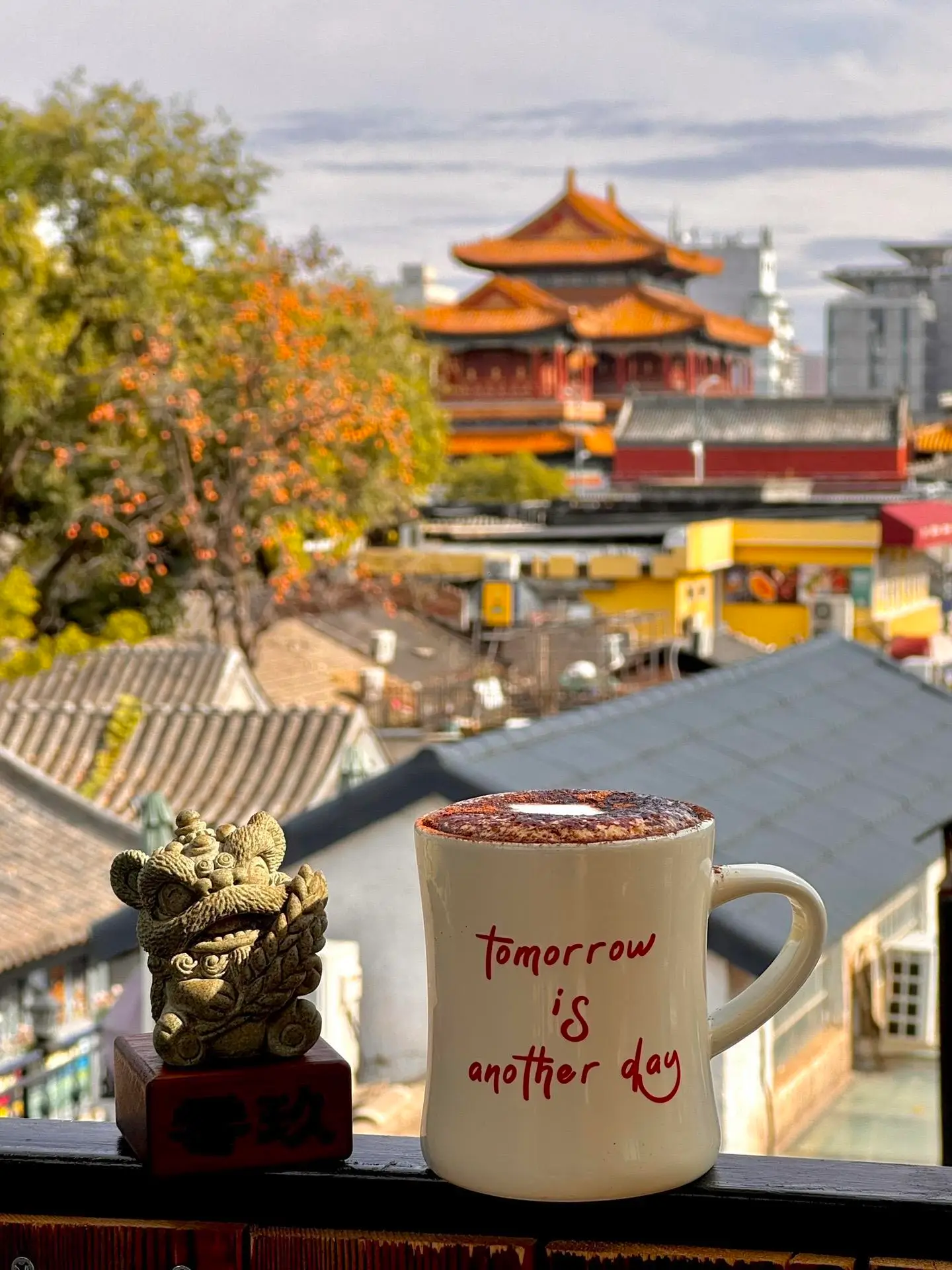 A coffee cup on a rooftop terrace near Lama Temple, overlooking hutong rooftops and the golden roofs of Yonghe Temple in Beijing.