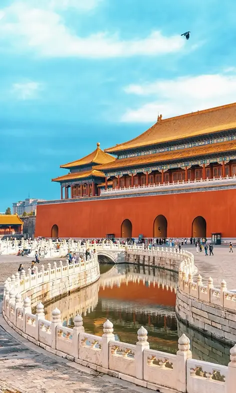 **Forbidden City in Beijing with red palace walls, golden roofs, stone bridge, moat, and visitors walking through the imperial palace complex.**