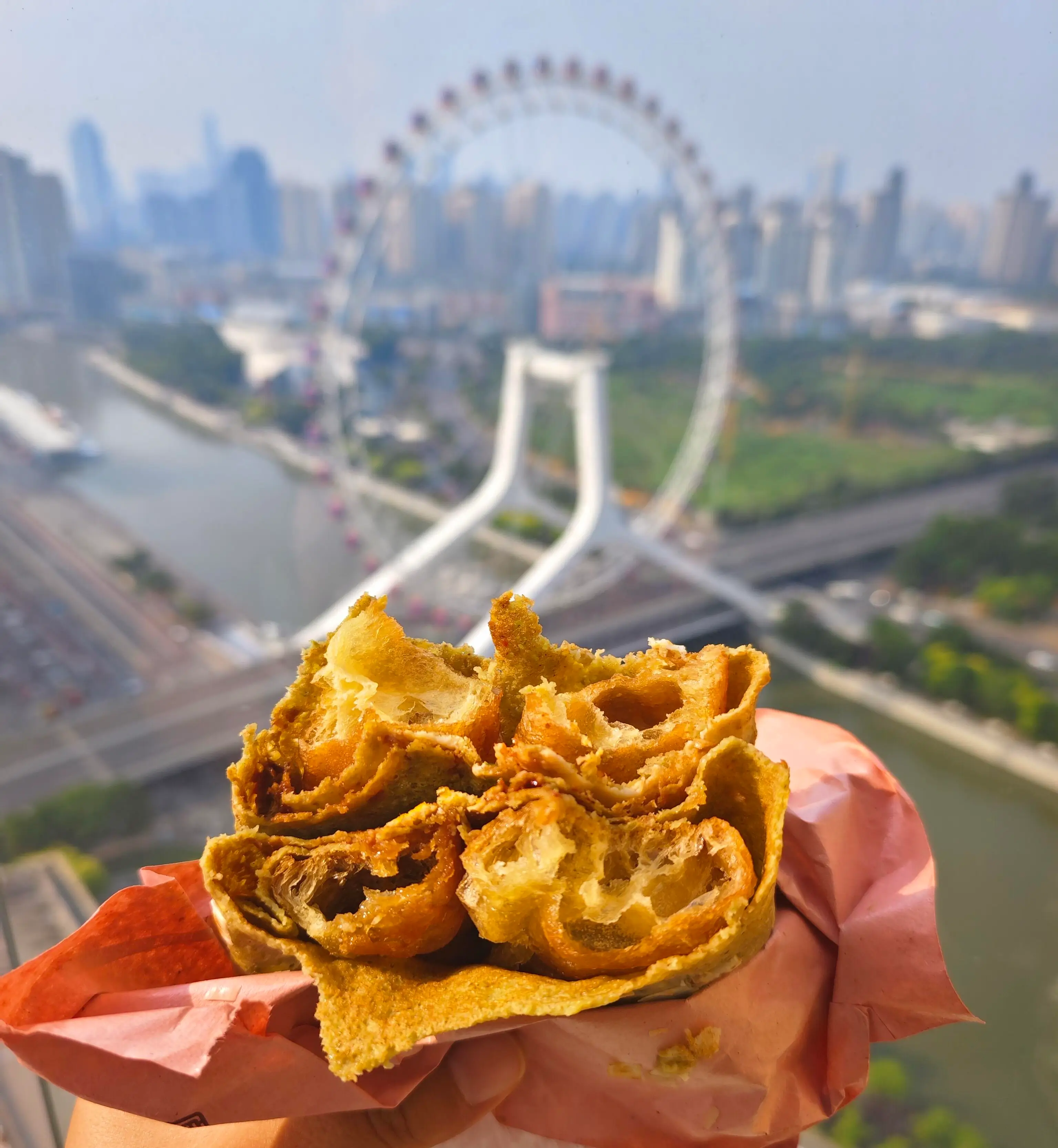 Tianjin jianbing guozi with crispy fried cracker served with a view of Tianjin Eye Ferris wheel in the background