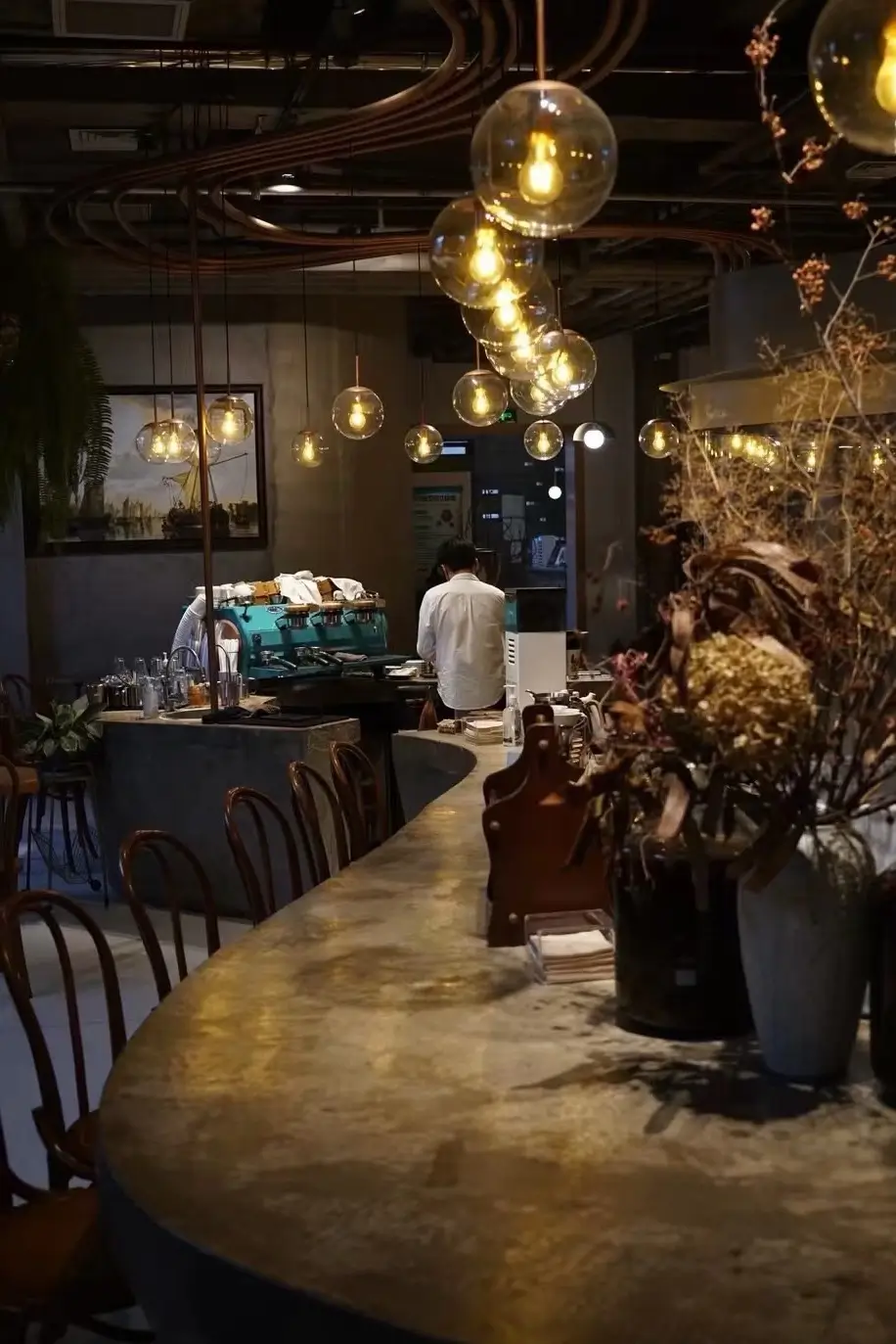 Cozy Beijing café interior at night with hanging glass pendant lights, marble bar counter, and barista working behind the espresso machine.