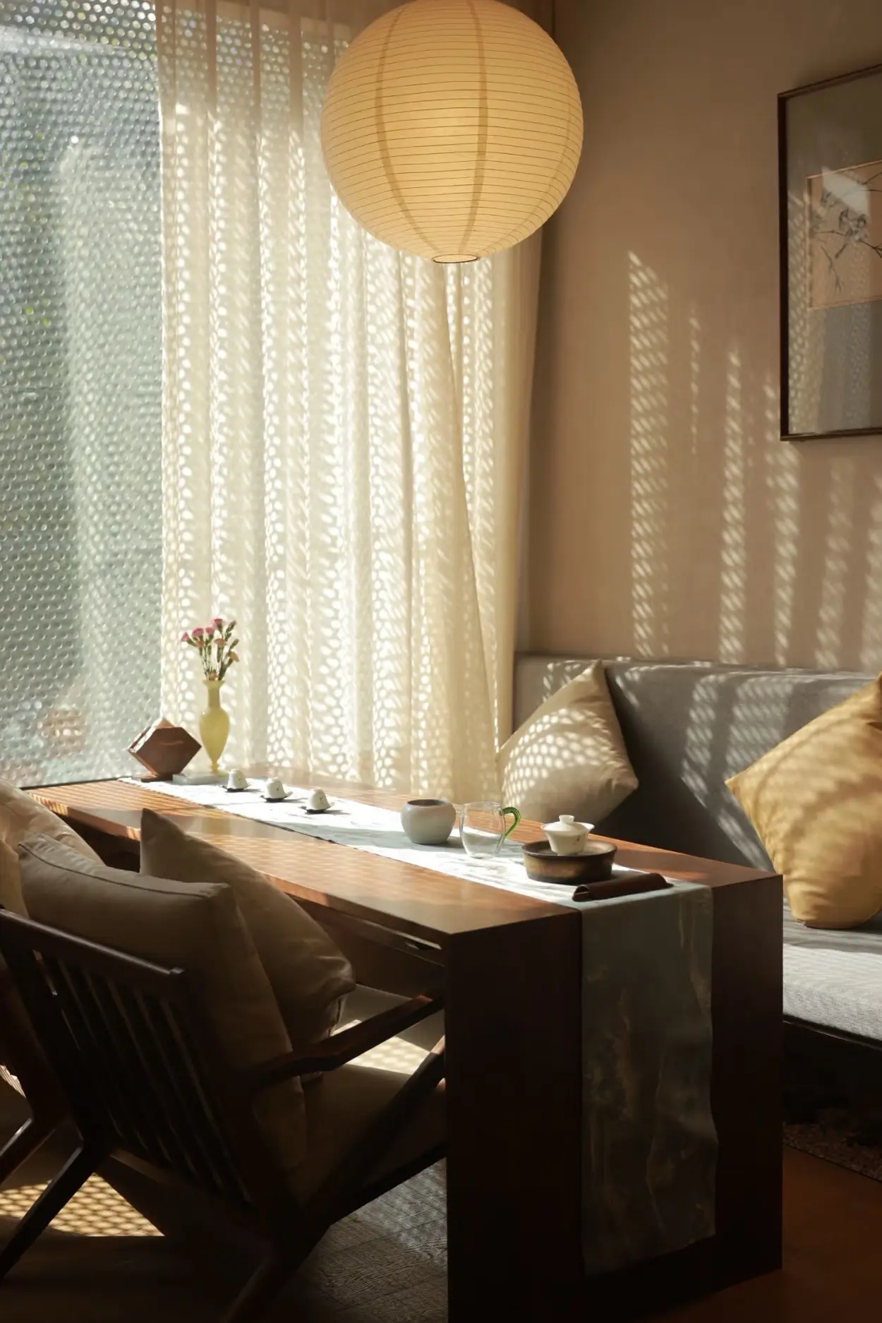 Sunlit tea corner with wooden furniture, cushions, and teaware beside sheer curtains creating a calm