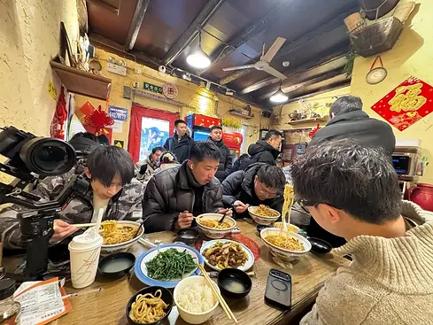 Local diners sharing noodles and classic Beijing dishes inside a lively hutong restaurant during a Bite Escape food tour.