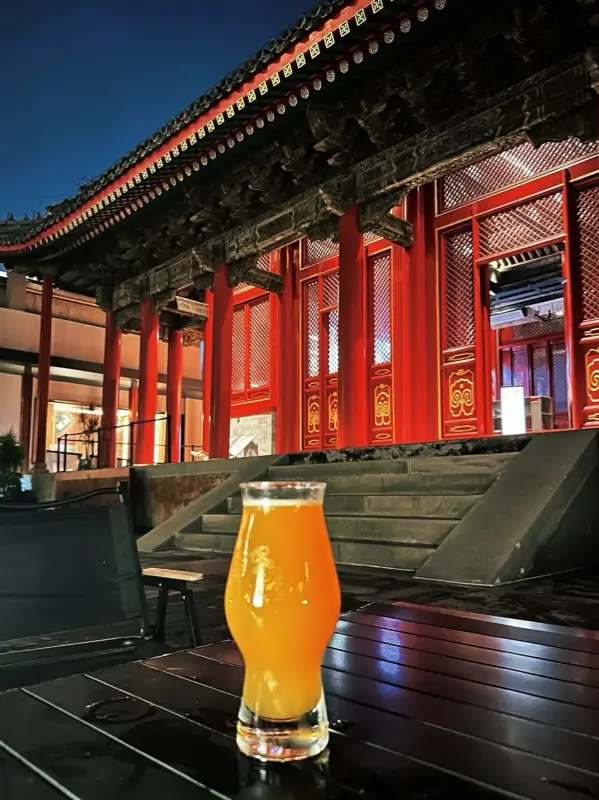 A beer glass placed on an outdoor table with traditional red pillars and rooftops in the background.