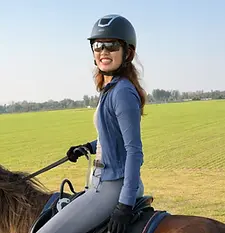 Bite Escape horseback riding coach riding in open countryside field with helmet and gloves