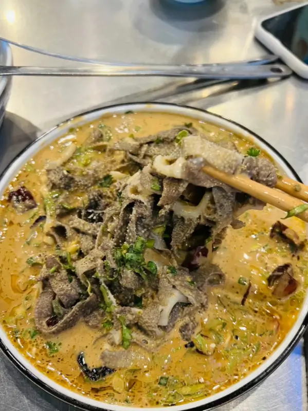 Close-up of boiled tripe (Baodu) being dipped in sesame sauce at Man Hen Ji.