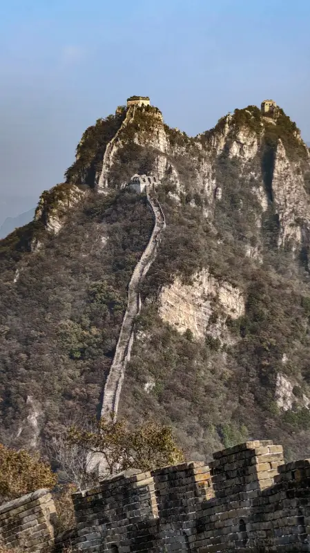 The wild Great Wall running up a steep mountain ridge under a clear sky.