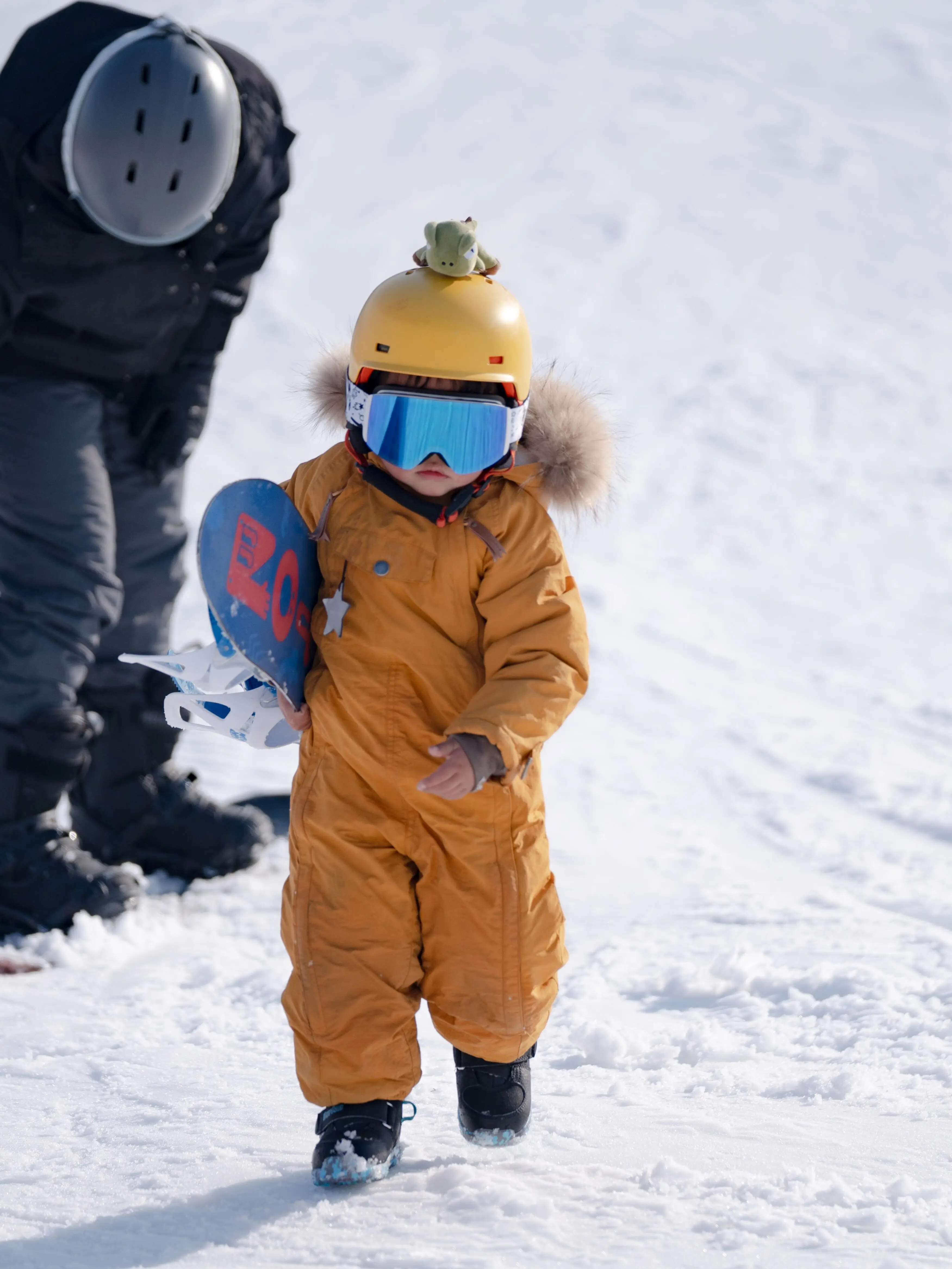 Young child learning to snowboard in Beijing, dressed in winter gear on a snowy slope
