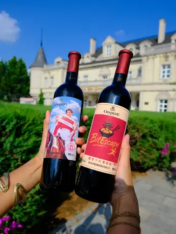 Two personalized Changyu red wine bottles with custom photo and Bite Escape labels held in front of Changyu Chateau AFIP in Beijing.