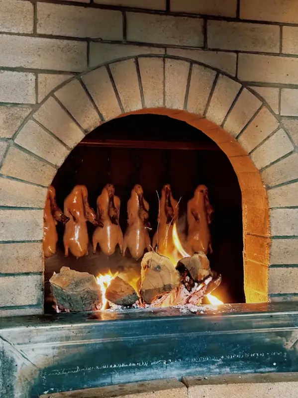 Peking duck roasting in a traditional open oven with hanging ducks