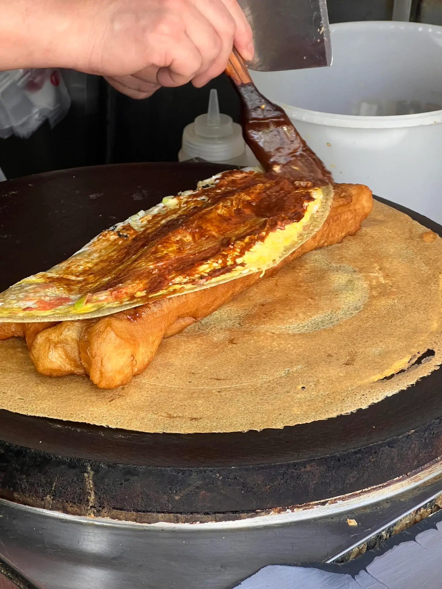 Freshly made Tianjin jianbing guozi, a traditional Chinese breakfast pancake prepared with egg, sauces, and crispy toppings