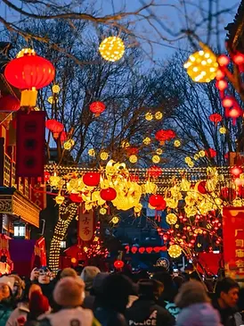 Festive lanterns glowing above Dashilar street in Beijing, with red lanterns and warm lights hanging over a crowded evening walkway.