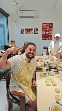 A traveler wearing a “China” apron smiles during a Beijing hutong baozi-making class, with freshly made buns and cooking ingredients on the table.