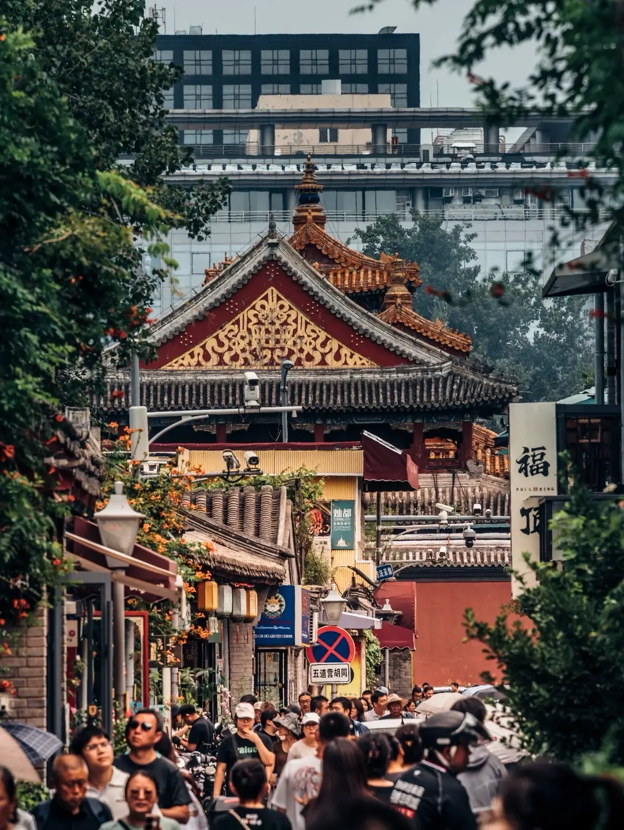 Crowded Beijing hutong street leading toward a historic temple with traditional Chinese roof details