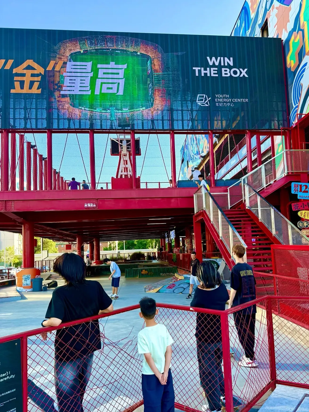 Red industrial-style structure at THE BOX Youth Energy Center in Beijing with a basketball court and young people hanging out, showcasing the mall’s creative, youth-focused lifestyle space.