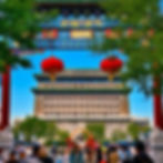 The majestic Zhengyangmen (Qianmen) Gate in Beijing framed by a traditional colorful Chinese archway with red lanterns and vibrant greenery.