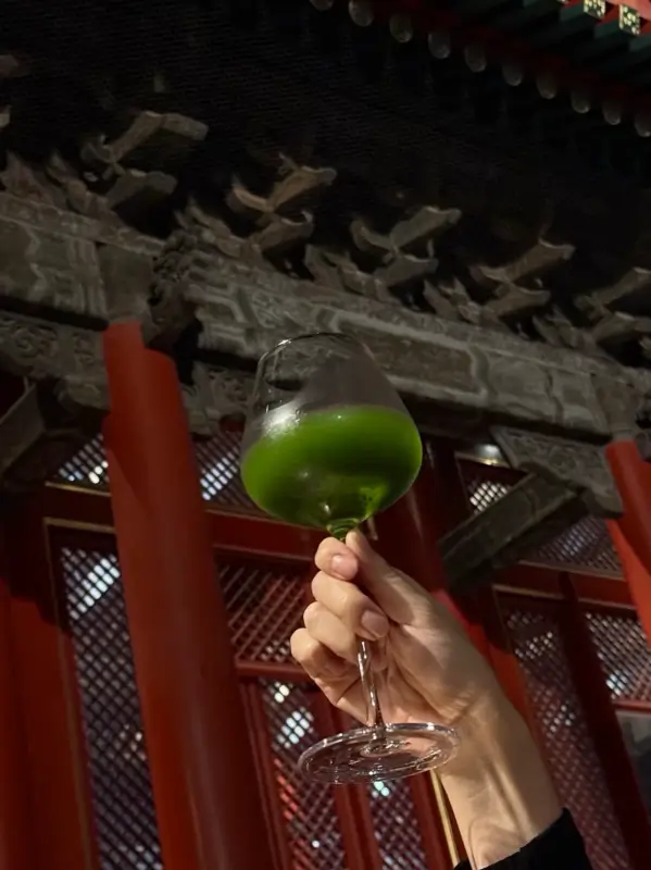A hand holding a drink under traditional wooden eaves at night.