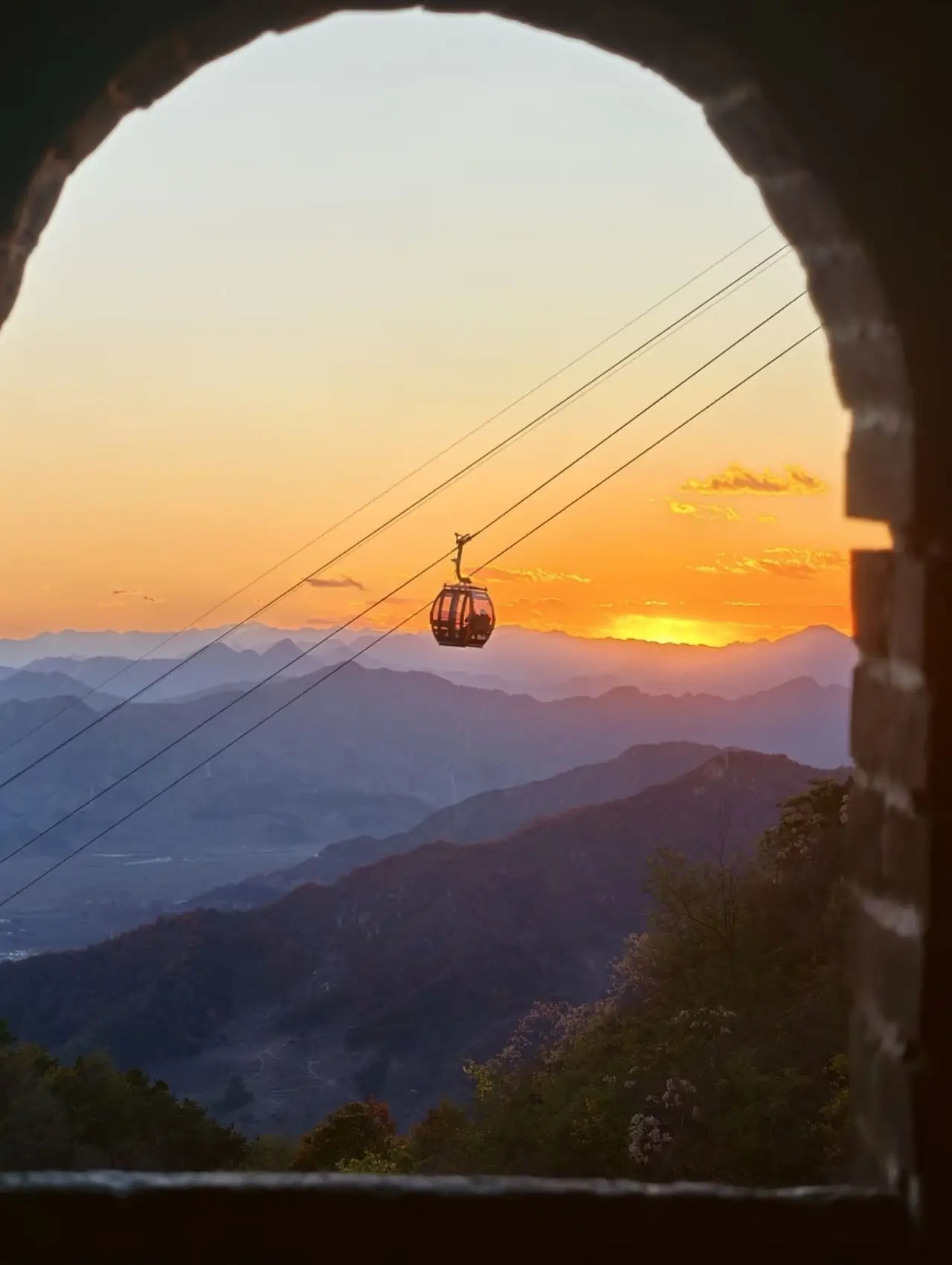 Cable car gondola at sunset over mountain ridges near the Great Wall, with warm golden light and layered hills in the distance.