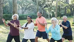 A small group practices Tai Chi outdoors in a green park setting, smiling and moving in sync during a Temple of Heaven cultural visit experience with Bite Escape