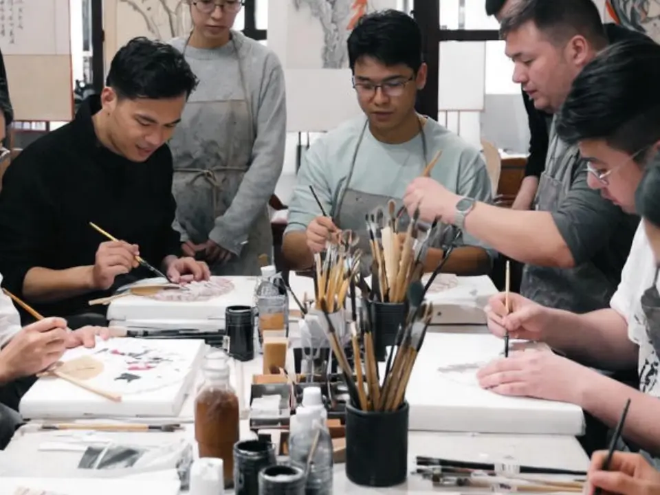 A group of students practicing traditional Chinese calligraphy and brush painting in a studio.