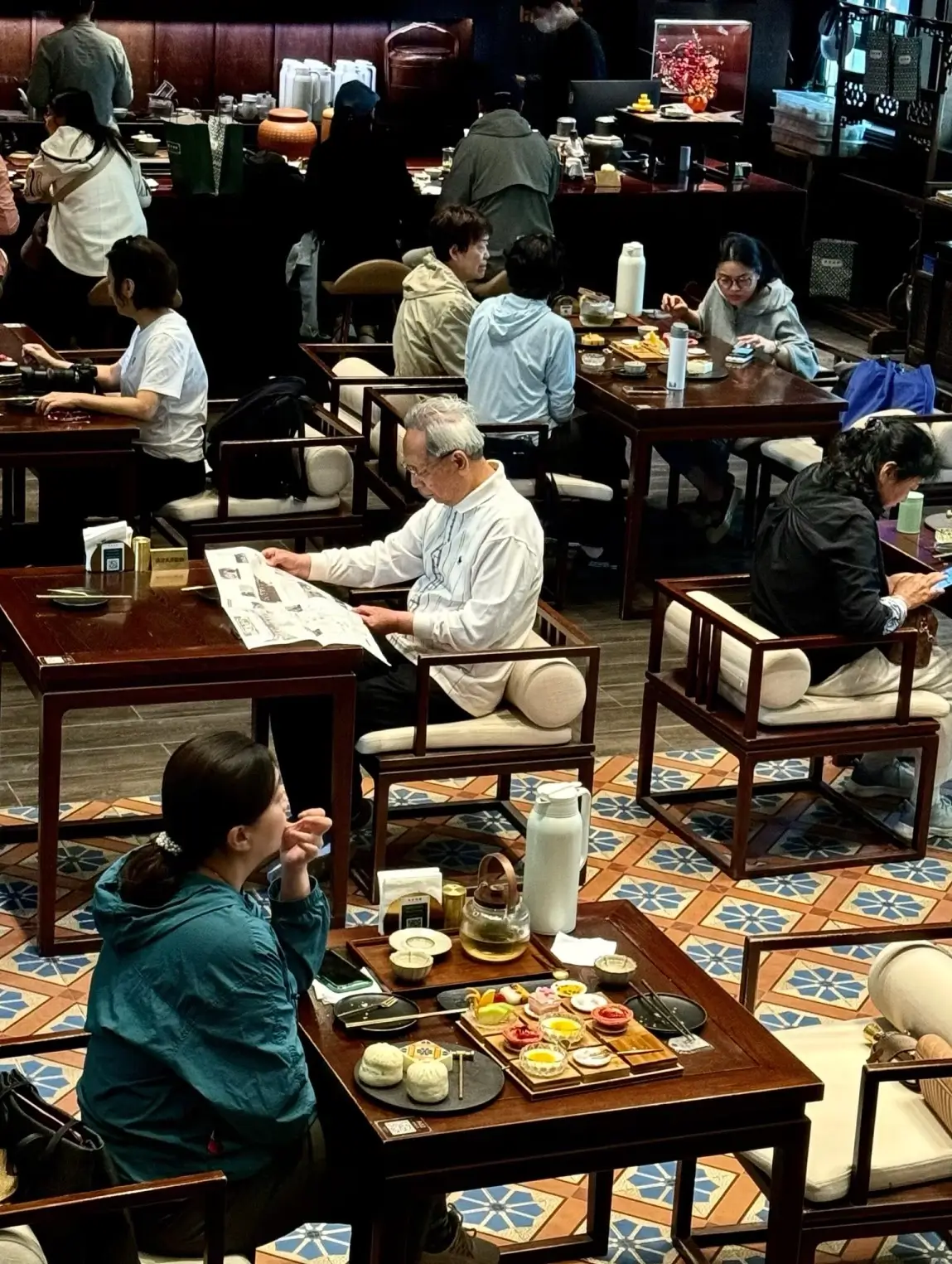 People quietly reading newspapers and drinking tea inside a classic Chinese teahouse with wooden fur