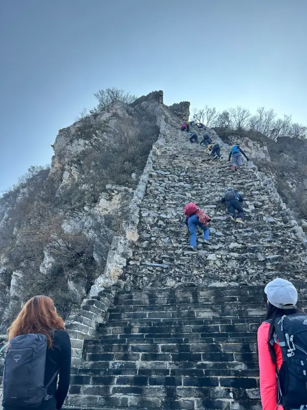 Hikers climbing a very steep, broken stone staircase on the wild Great Wall.