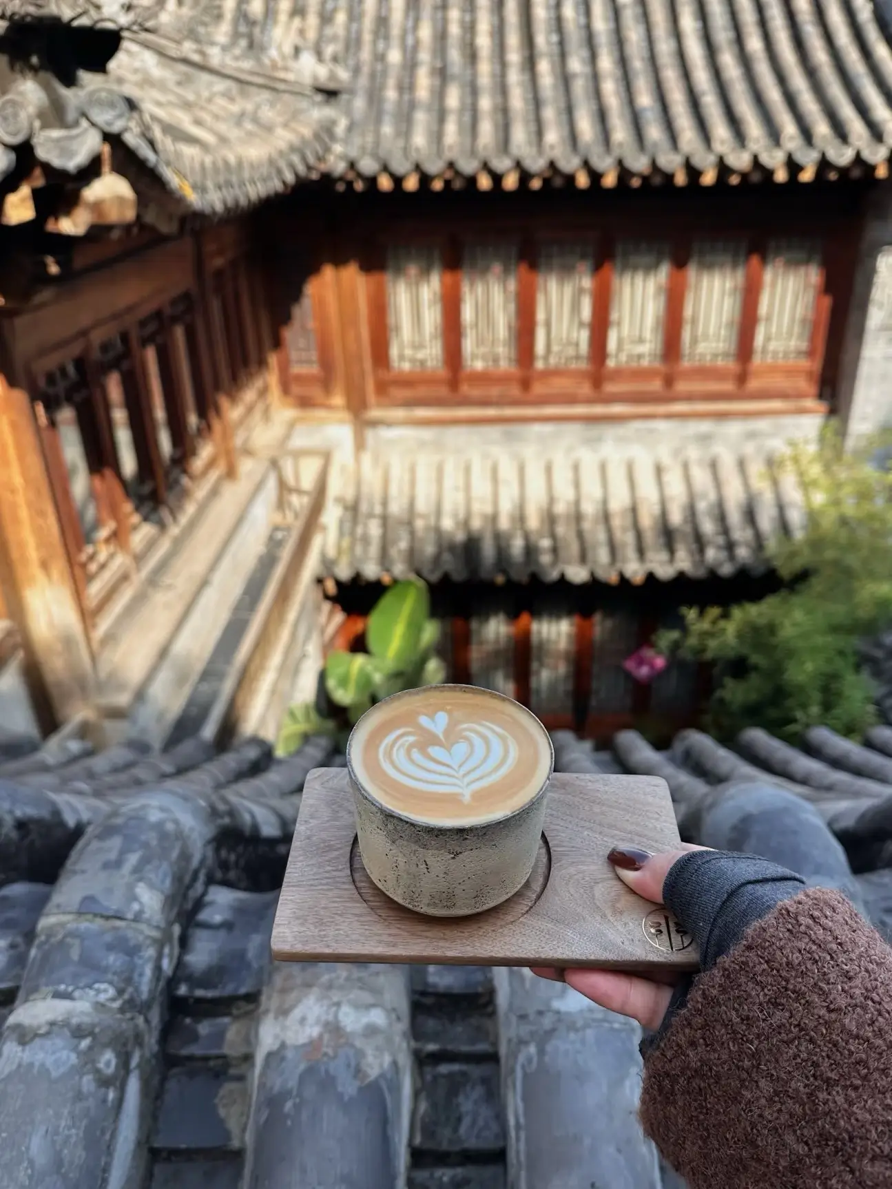Latte served on a wooden tray overlooking a traditional Beijing courtyard house, with tiled rooftops and wooden windows in the background.