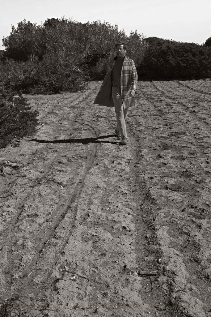 a man in a plaid coat walks down a dirt road