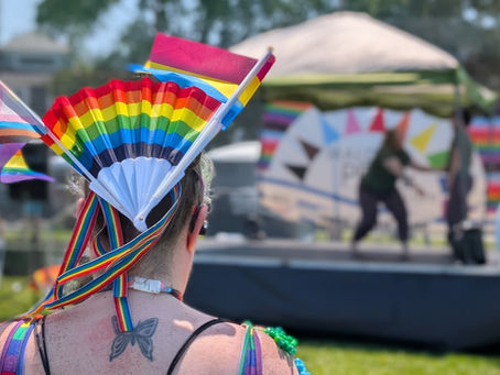 A person wearing pride-inspired clothing and decorations watching a dance group on stage at Malden Pride