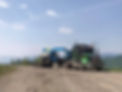 Green semi-truck hauling blue excavator on dirt road