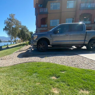 Gray pickup truck parked on gravel by a waterfront lawn