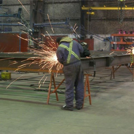 Worker grinding a metal beam in a steel fabrication shop